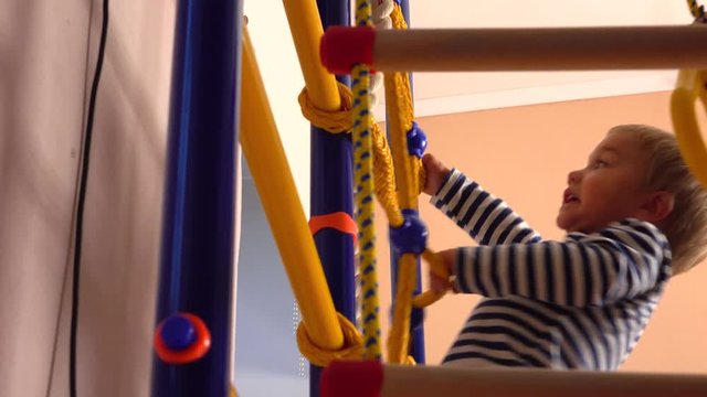 Happy little blond boy climbs up the ladder in playroom. Kid sport, success or achievement concepts. 4K video