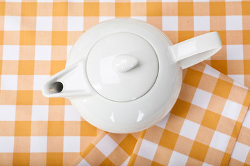 top view of a white teapot on a yellow checkered tablecloth
