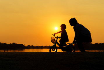 silhouette of a mother who teaches daughter to ride a bike.