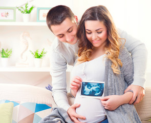 Happy young couple expecting baby. Beautiful pregnant woman and her husband together holding ultrasound picture of their baby