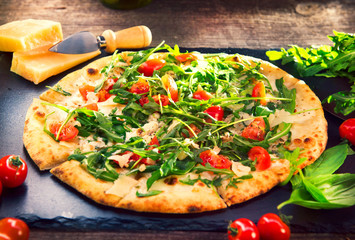 Pizza Caprese with arugula, cheese, yoghurt and cherry tomatoes closeup