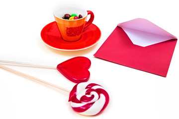 Orange cup with colorful button-shaped chocolates, red envelope and lollipops on the white background. 