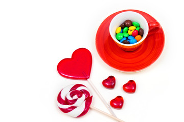 Orange cup with colorful button-shaped chocolates and lollipops on the white background. 