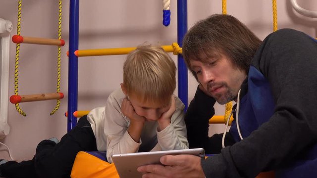 Dad and his little son watching cartoons on tablet computer together. Togetherness or parental control concepts. 4K video