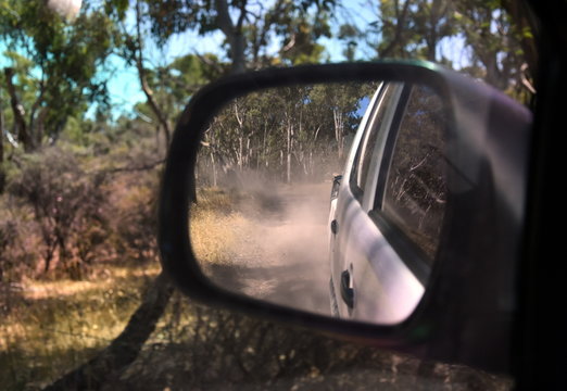 Reflections in a side view mirror of a car driving in the bush. Rear view car mirror in forest live green. Dirt road leading up to a slavery plantation. Concept of 4wd off-road driving in the nature.