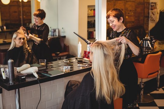 Female hairdresser styling clients hair in salon