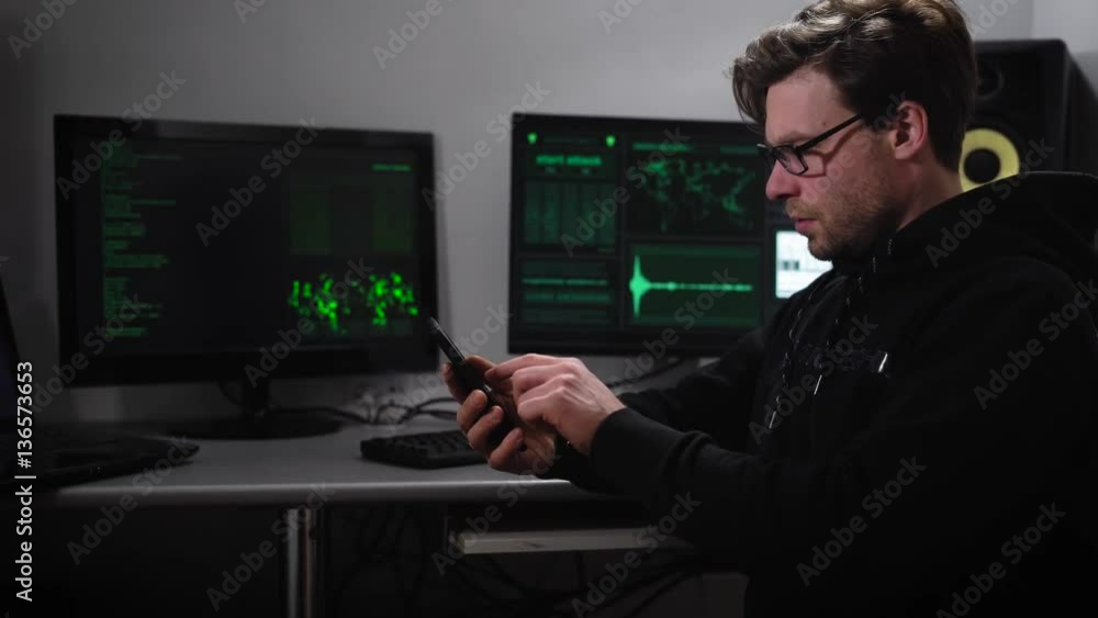 Poster a hacker in the computer room. a man in sunglasses and with a smartphone on hand trying to hack info