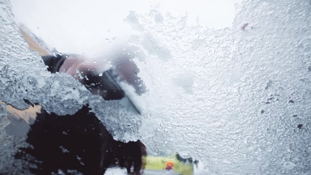 Close up shot of a person removing the ice from a car's frozen windshield, with and ice scraper.