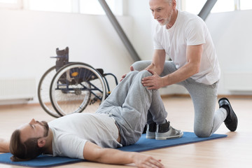 Skilled aged orthopedist stretching the disabled person in the gym