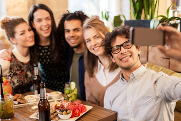 friends taking selfie by smartphone at bar or cafe