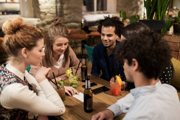 happy friends with drinks and bill at bar or cafe