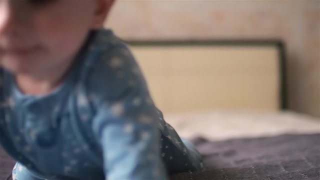 Lovely smiling baby boy with dimples on cheeks and in star pyjamas crawling on bed