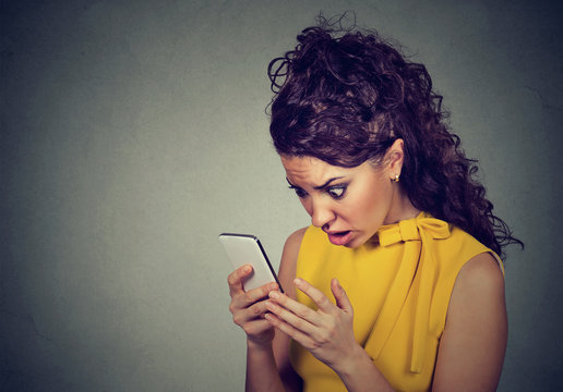 Shocked woman looking at mobile phone with cross face expression