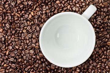 Overhead shot of an empty white cup over over a fresh background of whole coffee beans. Flat lay top view style.