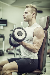 Fototapeta na wymiar Handsome young man training biceps lifting dumbbells on bench in a gym