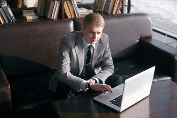 elegant businessman sitting on the sofa at the table. the hand is on the laptop and looking into the distance.