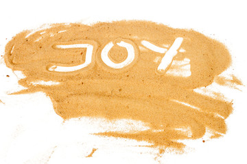 Word JOY written on pile of yellow sand