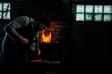 The blacksmith manually forging the hot metal on the anvil in smithy with spark fireworks