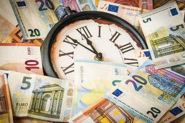 Fuenf Minuten vor zwoelf Uhr / Euro Geldscheine und eine Uhr, die Zeiger stehen fuenf Minuten vor zwoelf.