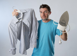 young attractive and frustrated man holding iron and shirt stressed and tired in bored and lazy face
