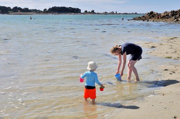 Un petit garçon cherche des coques avec sa mère à marée basse sur une plage de Bretagne