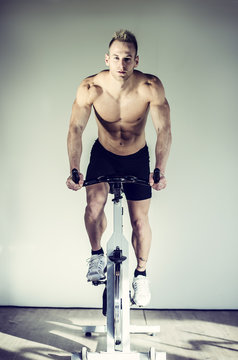 Attractive young man exercising in gym, spinning on stationary bike