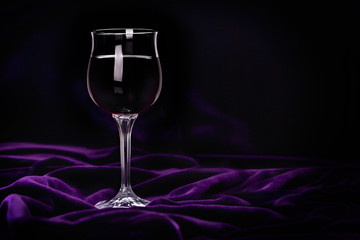 Glass of red wine on purple rippled velvet fabric.