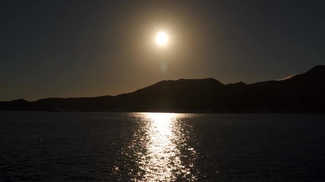 The outline of the mountains against the setting sun. The sun reflected in the Sea