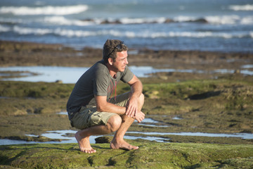 Man sits on his honches on rocks by ocean