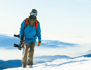 Fototapeta na wymiar Young snowboarder in helmet walking at the top of a mountain with his snowboard in hand