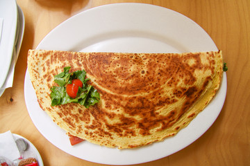 Pancake stuffed with tomato, cheese and green salad on white plate. Top view