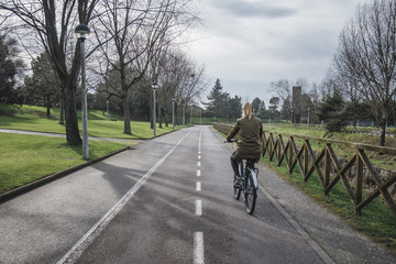 Obraz premium A beautiful blonde woman riding a bicycle along a bike path in a city park