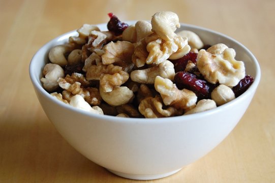 white ceramic bowl full of walnuts, cashew nuts and dried cranberries  