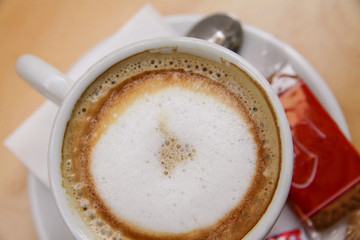 Cappuccino coffee in white cup servired with sugar and bisquit. Top view . Close up