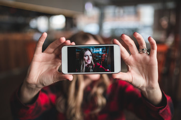 Beautiful young woman sitting in cafe and taking selfie photo.