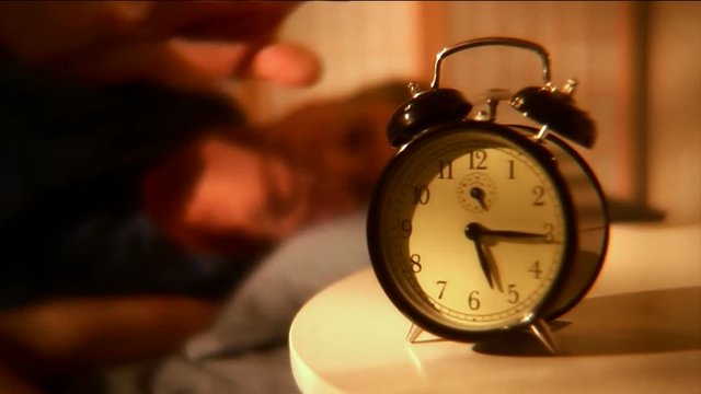 Rack focus of a man reaching for the alarm clock to turn it off  then rolls over.
