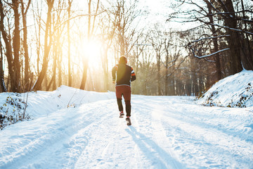 View of sportsman running in snowy forest at wonderful sunrise