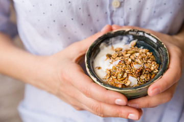 Young woman with muesli bowl. Girl eating breakfast cereals with nuts, pumpkin seeds, oats and yogurt in bowl. Girl holding homemade granola. Healthy snack or breakfast in the morning.