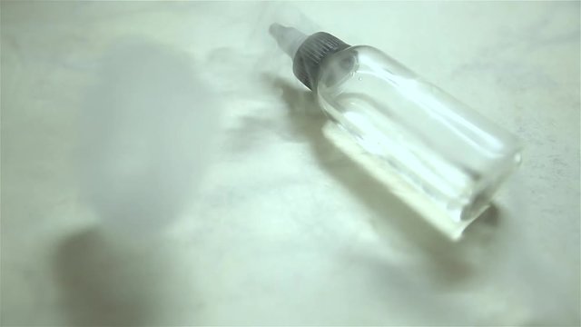 Bottle with liquid and flavor for electonic cigarette stay on the table. A lot of steam for background.