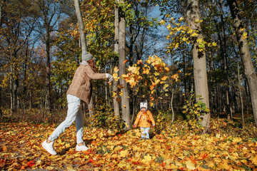 mother throws autumn leaves on daughter in the park