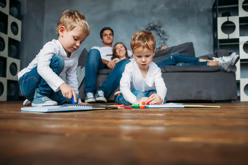Children draw markers on floor while parents relax couch