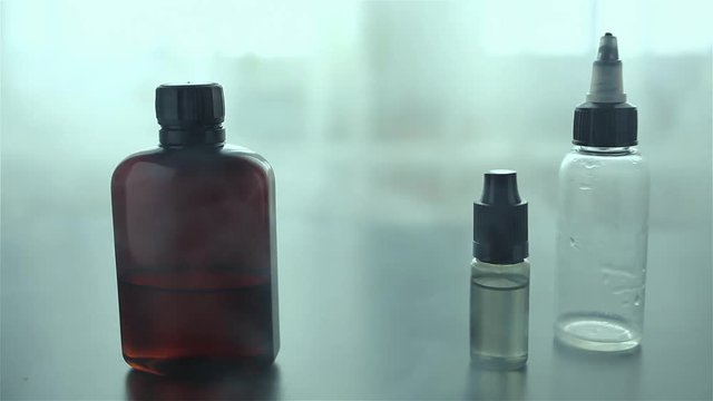 Bottles with liquid and flavor for electonic cigarette stay on a black wooden table. A lot of steam for background.