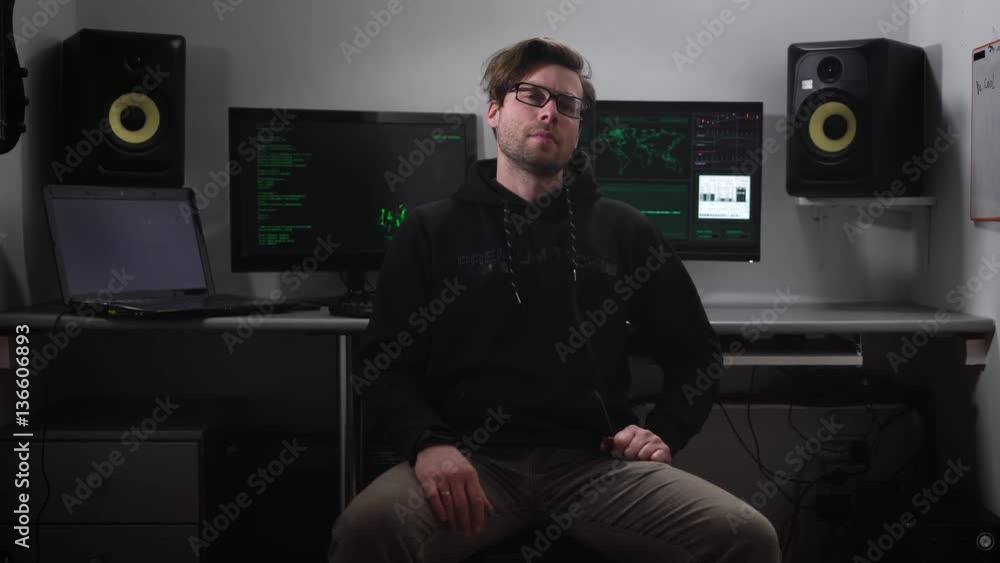 Poster young man with glasses wearing a dark jacket fixedly looking into the camera and then folds his hand