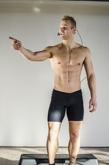 Fototapeta premium Young aerobics male coach shirtless leaning on step teaching class, looking at camera