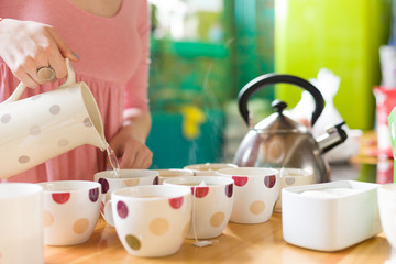 Closeup of cute tea set and woman's hand pouring hot water into a cup. Tea ceremony. Birthday party and tea with cake.