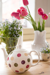 Obraz na płótnie Canvas Teapot with dots and vases with beautiful spring flowers on the wooden table. Decoration for home interior. Forget-me-not and tulips in vases. Flowers from the garden.Tea time and table setting.