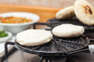 Colombian arepas being roasted on a round grill