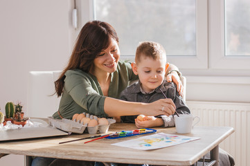 Mom and her son painting eggs together at home, Easter preparation