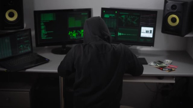 Hacker thinks about how his hack program and then abruptly turns to the monitor screen and starts working. He is wearing a black hoodie, hood hides his head, but some bangs falls on the hair.
