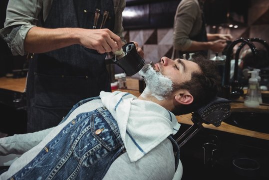 Mid section of barber applying cream on clients beard